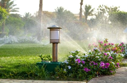 Plastic sprinkler irrigating flower bed on grass lawn with water in summer garden. Plastic sprinkler irrigating flower bed on grass lawn with water in summer garden.